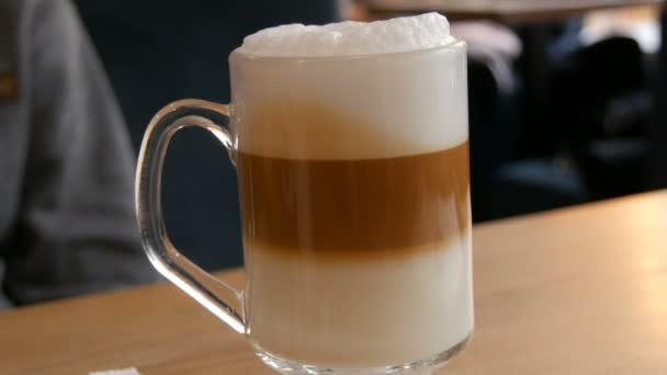 Finom frissen készített latte az asztalon egy kávézóban. Tejeskávé hab átlátszó, hosszú, speciális pohárban. - Felvétel, videó