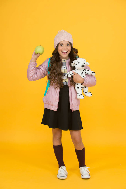 Regular day at school. Happy child yellow background. Warm clothes for cold season. Fashionable girl looks like hipster. Small girl winter hat. Trendy schoolgirl wear jacket skirt and long socks - Fotografie, Obrázek