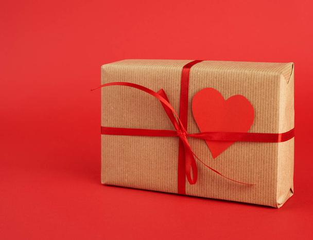 quadratische Schachtel mit einem Geschenk in braunem Bastelpapier und gebundenem Witz - Foto, Bild