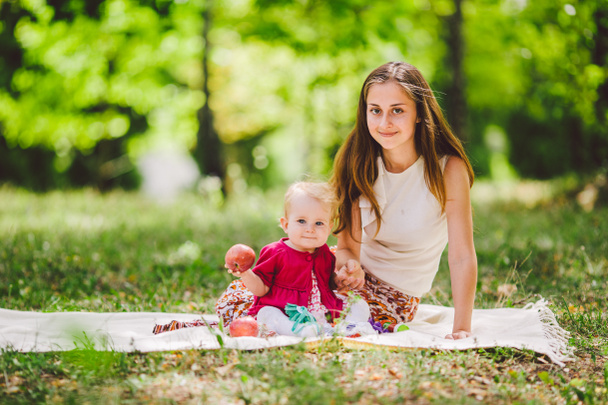 Mladá krásná matka s dcerou leží v parku na kostkovaném plotě. Rodinná venkovní rekreace. Rodinný letní piknik v parku. Máma a dcera na pikniku. Happy Family On Nature - Fotografie, Obrázek