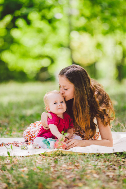 Young pretty mother with daughter lie on a plaid in the park. Family outdoor recreation. Family summer picnic in the park. Mom and daughter on picnic. Happy Family On Nature - 写真・画像