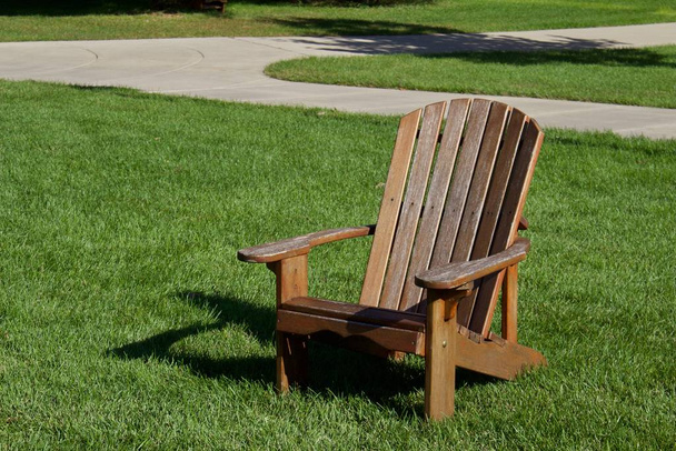 Vista de cerca de un sillón marrón Adirondack en un césped cubierto de hierba en un día soleado
 - Foto, imagen