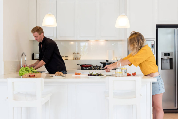 Pareja haciendo el almuerzo en una cocina de isla blanca en casa
 - Foto, Imagen