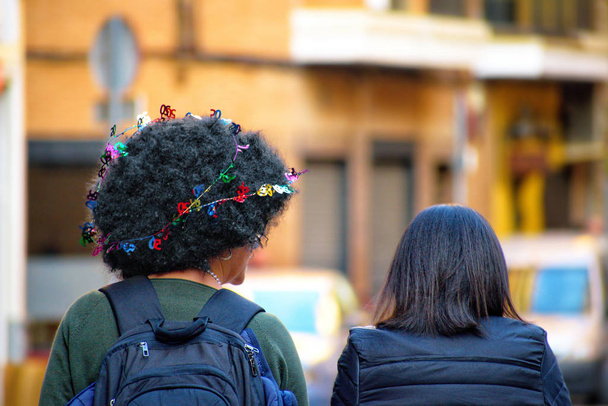Rear portrait of two woman walking at Murcia city. One of them with afro hair and exotic decoration and ornament on her hair. - Photo, Image