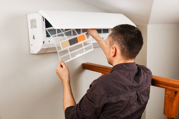 Male technician cleaning air conditioner indoors - Φωτογραφία, εικόνα