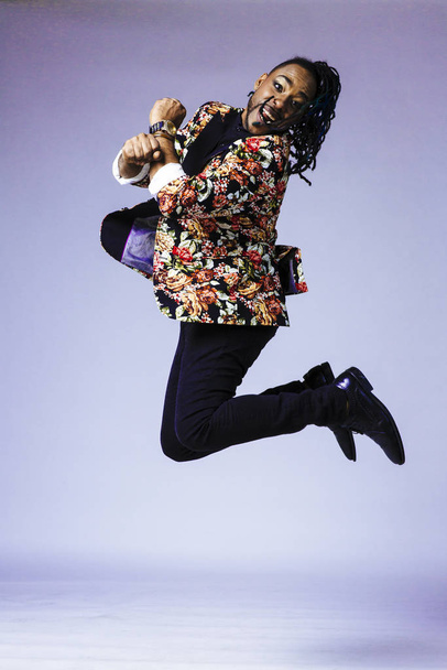 Retrato de estudio de un hombre con un traje estampado de flores y rastas saltando
 - Foto, Imagen