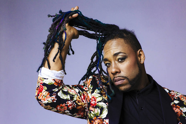 Studio portrait of a man wearing a flower patterned suit and dreadlocks playing with his hair - Photo, Image