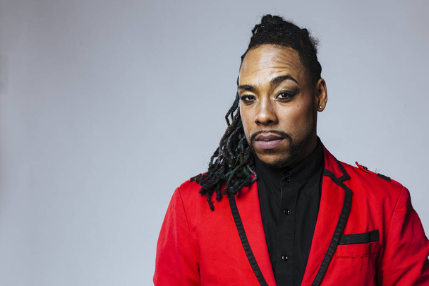Studio portrait of a man wearing a red jacket suit and dreadlocks - Photo, image