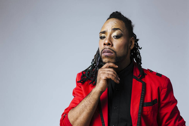 Closeup studio portrait of a man wearing a red jacket suit and dreadlocks thinking with hand on his face - Photo, Image