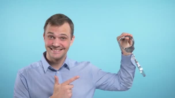 a man looks into the camera and shows the handcuffs. blue background - Imágenes, Vídeo