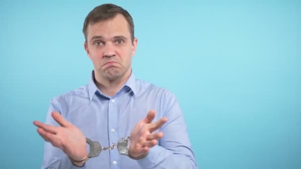 a man looks into the camera and shows the handcuffs. blue background - Metraje, vídeo