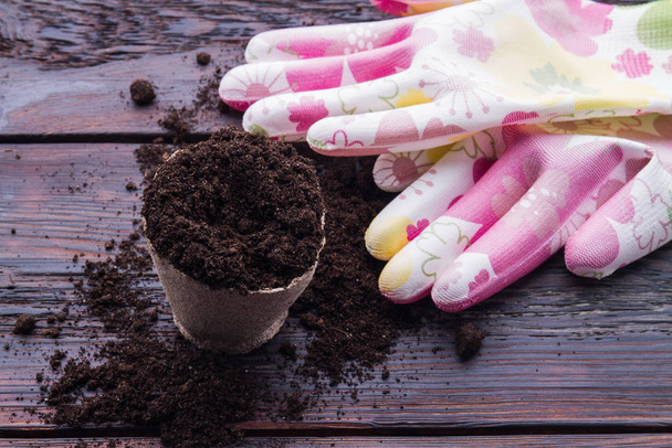 Круглая кастрюля с почвой и садовыми перчатками
. - Фото, изображение