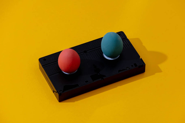 Two Easter eggs and VHS cassette on yellow background - Fotoğraf, Görsel