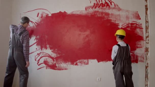 Een kleine jongen en zijn vader schilderen muren in rood - Video