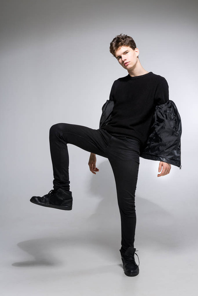 full length portrait of young fit man in dark cloths on the white background. Young Male Fashion Model Posing In Casual Outfit. Attractive young fashion model wearing black in leather jacket - Φωτογραφία, εικόνα