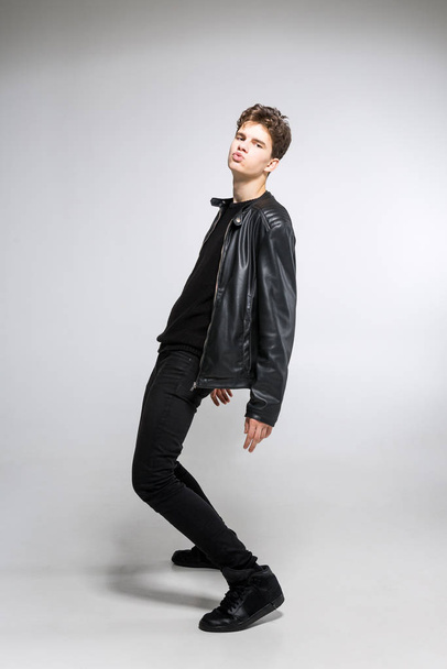 full length portrait of young fit man in dark cloths on the white background. Young Male Fashion Model Posing In Casual Outfit. Attractive young fashion model wearing black in leather jacket - Photo, image