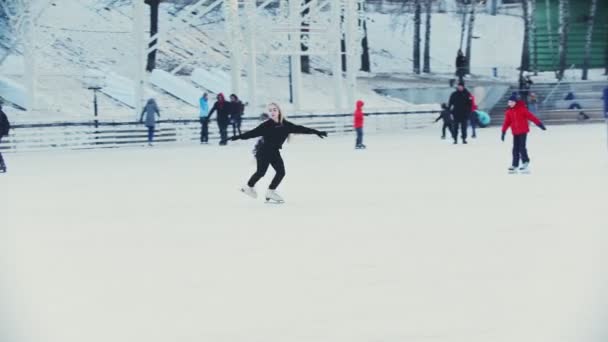 Egy fiatal szőke nő korcsolyázik a jégpályán mások körül. - Felvétel, videó