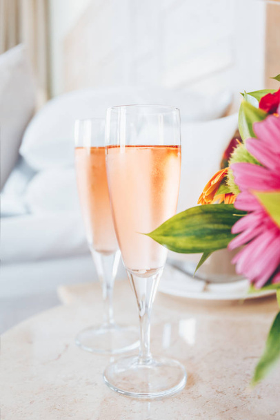 Two glasses of rose champagne in the upscale hotel room. Dating, romance, honeymoon, valentine, getaway concepts - Photo, Image