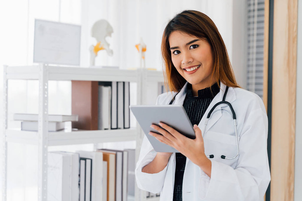 Asian medical woman enjoying work while browsing digital tablet at hospital - 写真・画像