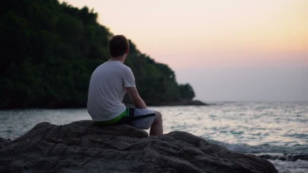 Depressziós fiatalember ül a sziklán a parton, miközben bámulja az óceánt. - Felvétel, videó
