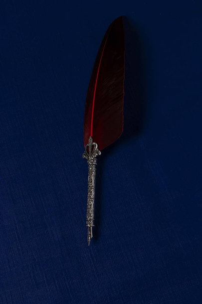 Pluma para escribir antigua de punta de plata con pluma de ave roja sobre un fondo azul clsico color en tendencia en el ao 2020 - Фото, изображение