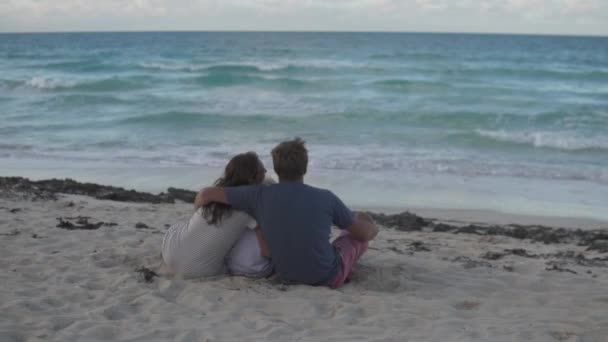 Rodina sedí zády ke kameře na pláži u oceánu - Záběry, video