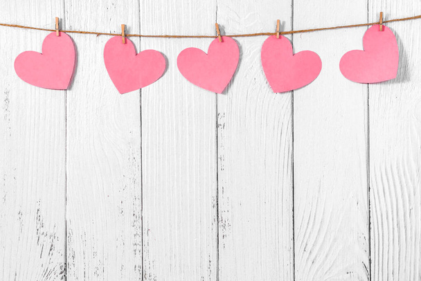 White painted wooden background with a garland of pink hearts. Natural rope and clothespins. Concept of recognition of love, romantic relationships, Valentines day in grunge style. Copy space - Φωτογραφία, εικόνα