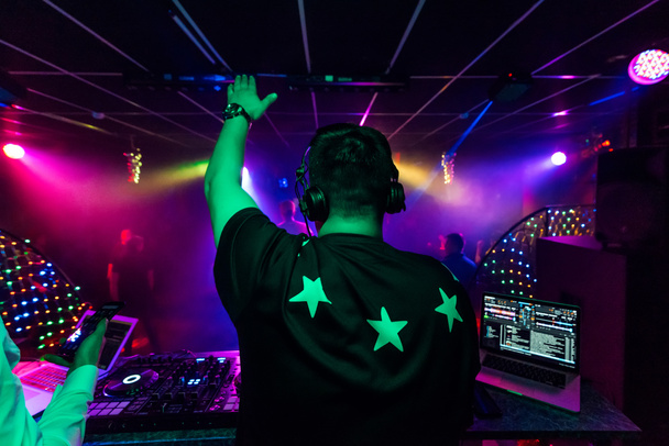 dos d'un DJ masculin avec une main levée dans un casque lors d'un concert électronique
 - Photo, image