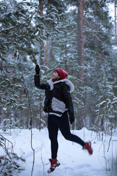 schöne attraktive Mädchen mit grünen Augen und roten Haaren spaziert gut gelaunt in einem verschneiten Winter-Wald - Foto, Bild