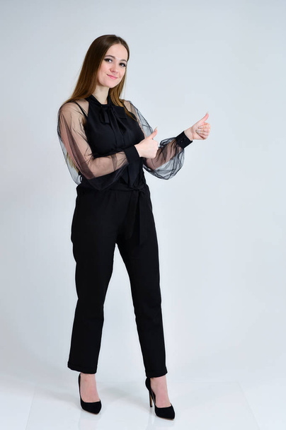 A full-length photo of a pretty smiling girl A brunette girl with excellent makeup in dark clothes is standing on a white background, talking with emotions. Concept portrait for a banner. - Fotografie, Obrázek