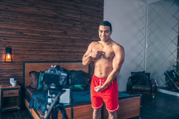 Young fit sportive vlogger in red shorts demonstrating his strong body - Foto, immagini