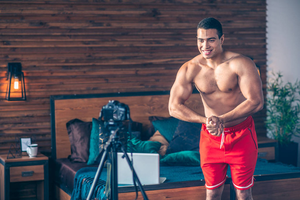 Young fit sportive vlogger in red shorts demonstrating his muscles to the camera - Fotoğraf, Görsel