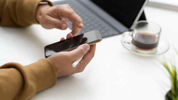 Oříznutý snímek textování na smartphone při práci v jednoduchém pracovním prostoru s tabletem a šálkem kávy  - Fotografie, Obrázek