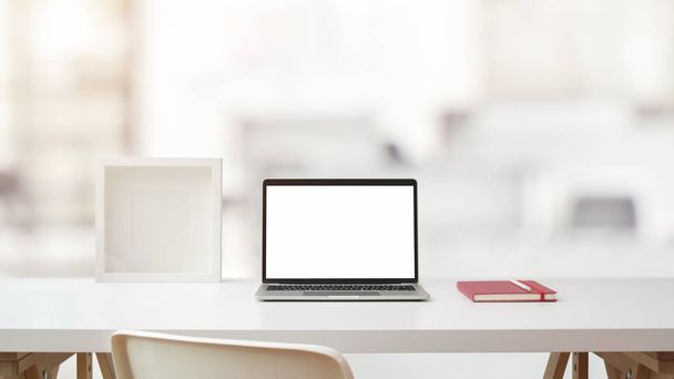 Закрыть вид на рабочее пространство с ноутбуком с открытым экраном, рамкой и ноутбуком на белом столе с размытой офисной комнатой
  - Фото, изображение