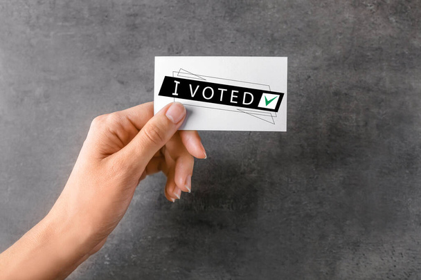 Mujer sosteniendo la tarjeta con texto I VOTED sobre fondo gris
 - Foto, imagen