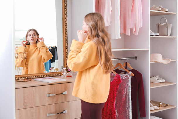 Beautiful young woman choosing accessories in her dressing room - 写真・画像