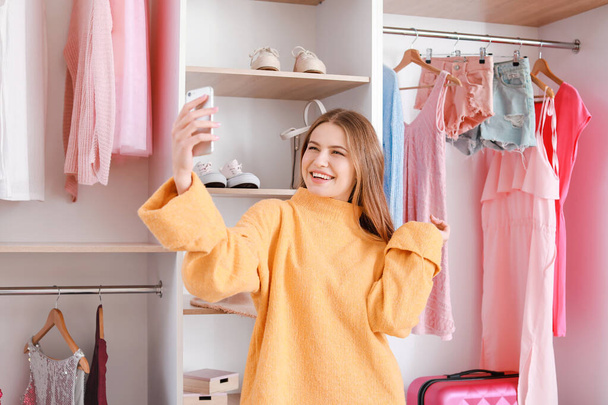 Mooie jonge vrouw het nemen van selfie in de buurt van grote garderobe - Foto, afbeelding