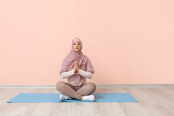 Sporty Muslim woman practicing yoga near color wall - Photo, image