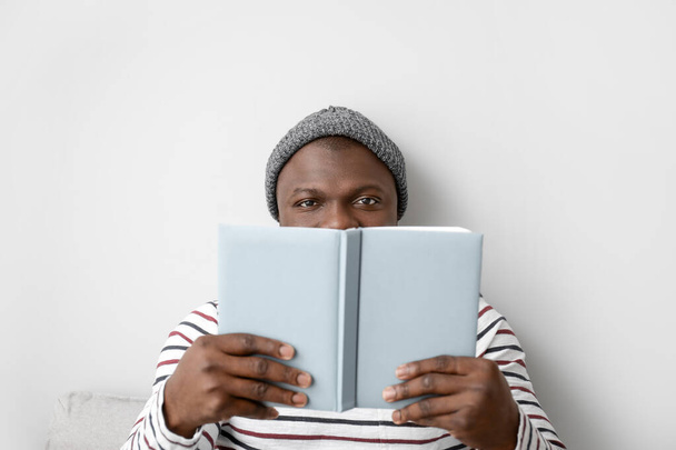 Hombre afroamericano leyendo libro sobre fondo claro - Foto, imagen