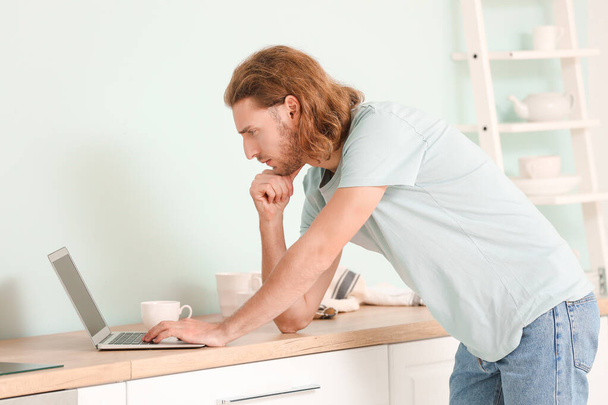 Handsome man with laptop in kitchen at home - Foto, afbeelding