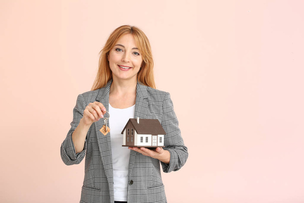 Female real estate agent with key and model of house on color background - Photo, image