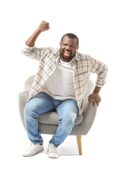 Emocjonalny Afroamerykanin ogląda telewizję siedząc w fotelu na białym tle - Zdjęcie, obraz
