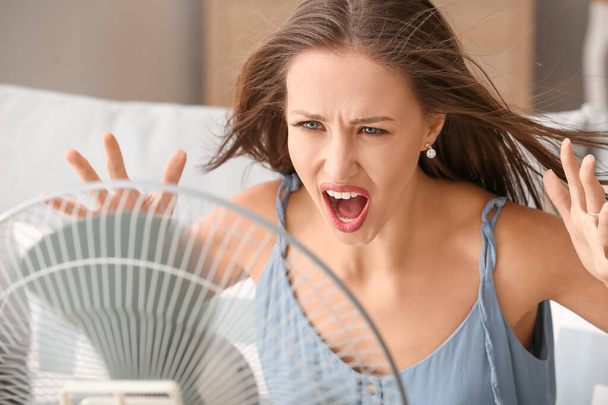 Злий жінка, що страждає від спеки біля електричного вентилятора вдома
 - Фото, зображення
