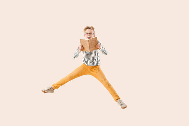 Skoczny chłopczyk z książką na jasnym tle - Zdjęcie, obraz