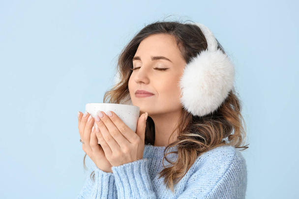 schöne junge Frau in warmem Pullover und mit heißem Tee auf farbigem Hintergrund - Foto, Bild