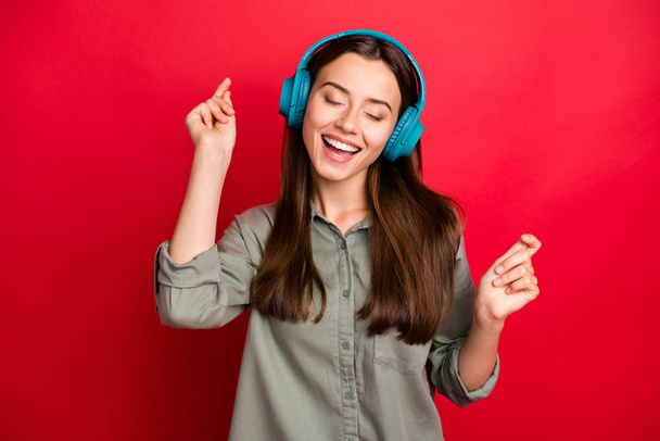 美しい女性の陽気なムードの写真耳の現代技術のヘッドフォンは、新しい人気の若者の歌を聞くカジュアルグレーの緑色のシャツを着用隔離された赤い色の背景 - 写真・画像