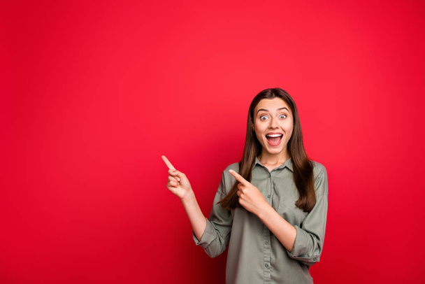 Portrait of her she nice attractive lovely cheerful cheery straight-haired girl in khaki shirt pointing copy space ad advert like isolated on bright vivid shine vibrant red color background - 写真・画像