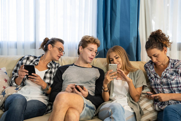 Groupe de jeunes gens habillés informellement assis sur un canapé dans une salle à manger regardant le mobile. Mode de vie - Photo, image