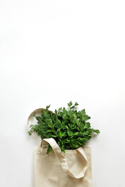 A bunch of fresh organic greenery parsley and dill in a cotton reusable bag on a white background. Healthy food, organic products, eco friendly lifestyle, zero waste concept. Top view, copy space. - Foto, Imagen