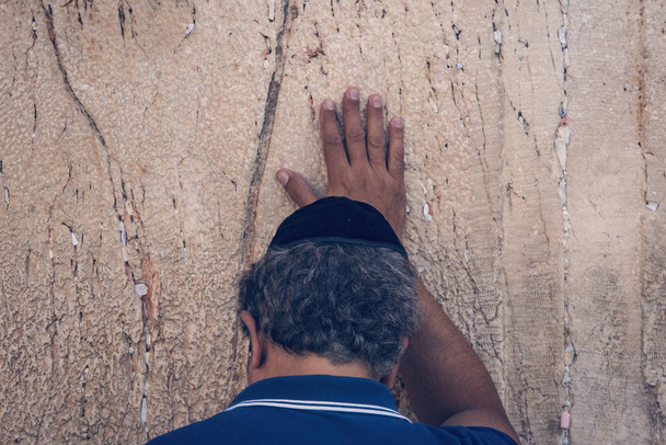 Joodse orthodoxe man bidt met sterke emoties in de buurt van de stenen van de westelijke muur, een van de grote oude Joodse relikwieën. Achterkant van het hoofd van een oude man die de kalkstenen muur aanraakt en bidt - Foto, afbeelding